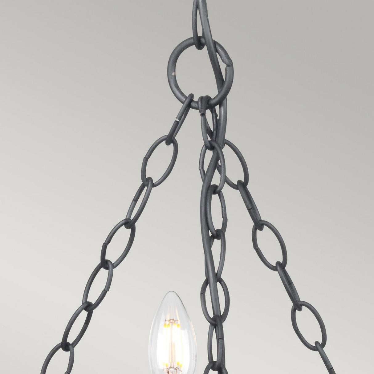 A close-up of a black metal chain suspending a vintage-style light bulb with a visible filament against a light gray backdrop. The design, inspired by medieval aesthetics, showcases large links and an exposed bulb, capturing the rustic charm reminiscent of the Saxon 5 Light Chandelier - Black.