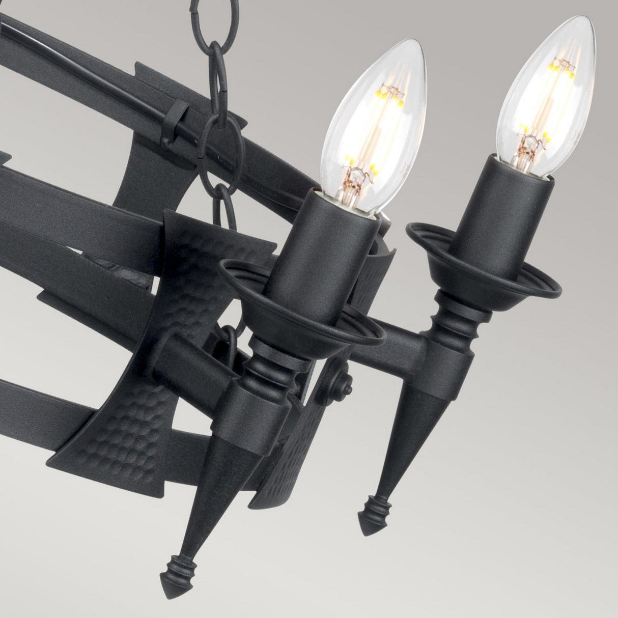 Close-up of the Saxon 5 Light Chandelier - Black, featuring a black wrought iron build with two exposed flame-shaped bulbs. Its spear-like arms and matte finish showcase a medieval-inspired design against a neutral background.