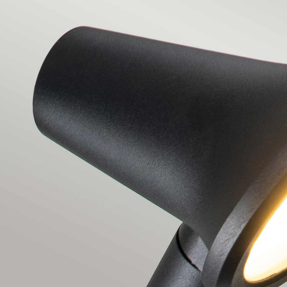 Close-up of a sleek, modern black Selma Outdoor LED Wall Light featuring an adjustable directional head and a cylindrical shade, illuminated at the edge, set against a light gray background.