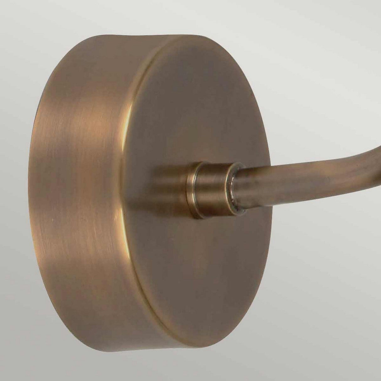 Close-up of the Sheldon 1 Light Outdoor Wall Light in aged brass, featuring a round base and curved arm. The brushed metal texture exudes industrial charm, set against a light gray background.