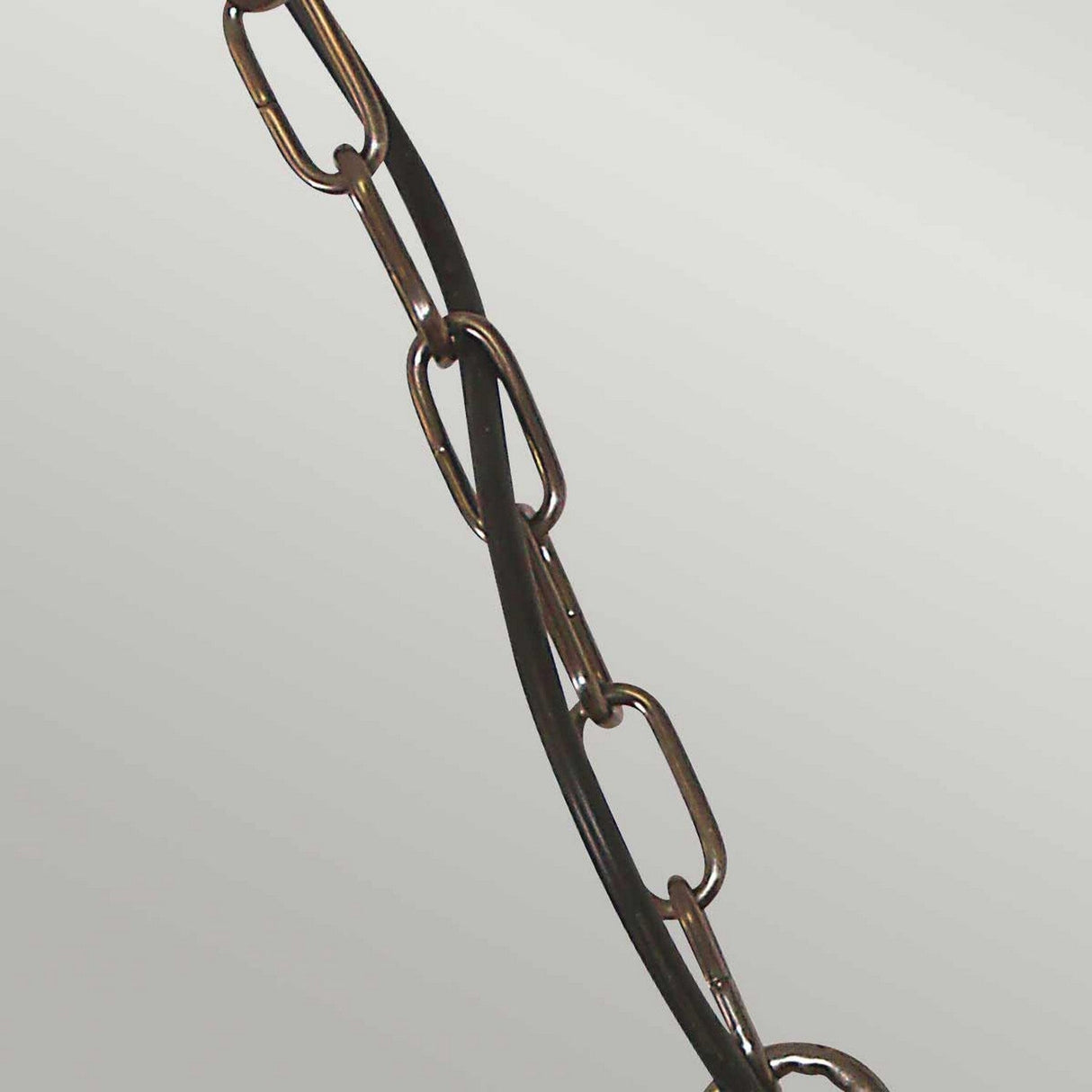 The Sheldon 1 Light Outdoor Chain Pendant in aged brass, with its interlocking metal links twisted with a black cable, exudes rugged charm. Set against a plain, light gray background, it enhances the piece's minimalistic and industrial aesthetic.