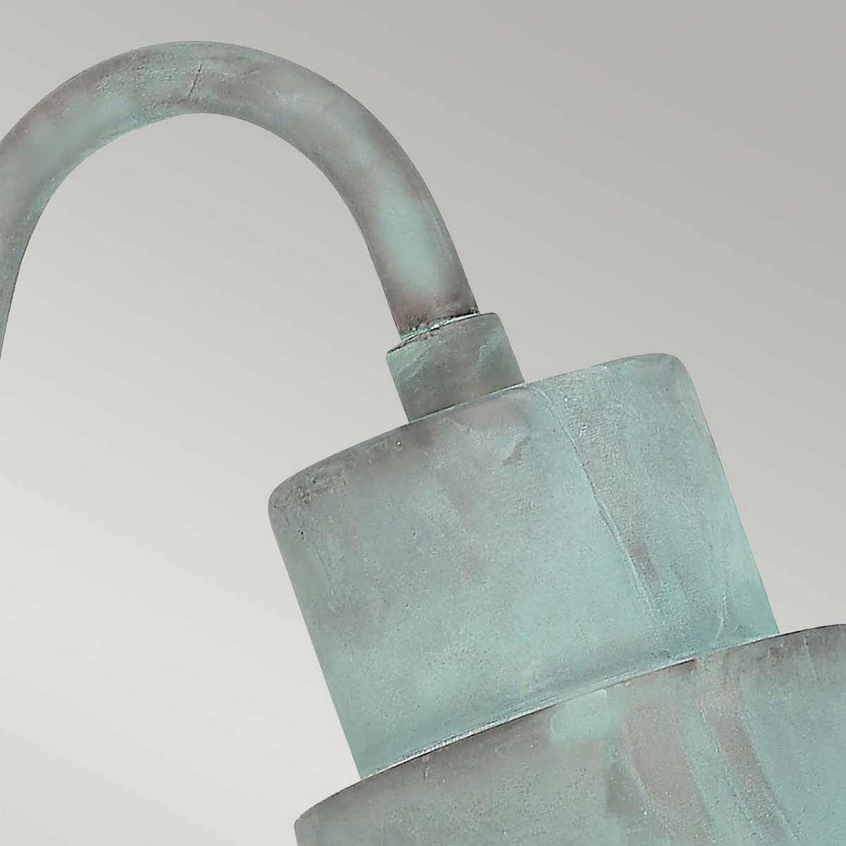 Close-up of the Sheldon 1 Light Outdoor Wall Light in verdigris finish, featuring a weathered, aged look with a curved arm. It stands out against a plain gray background.