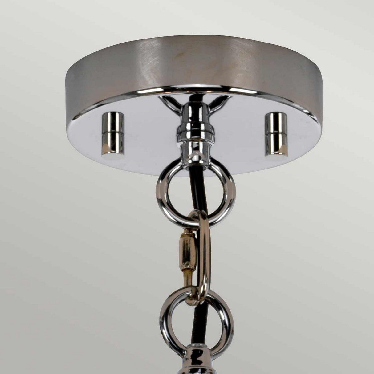 The close-up of the Shoal 4 Light Chandelier - Polished Nickel highlights a luxurious metallic ceiling fixture with a polished circular base. A chain elegantly descends, featuring intertwined links and a visible hanging mechanism, offering a sleek, shiny finish against a neutral background.