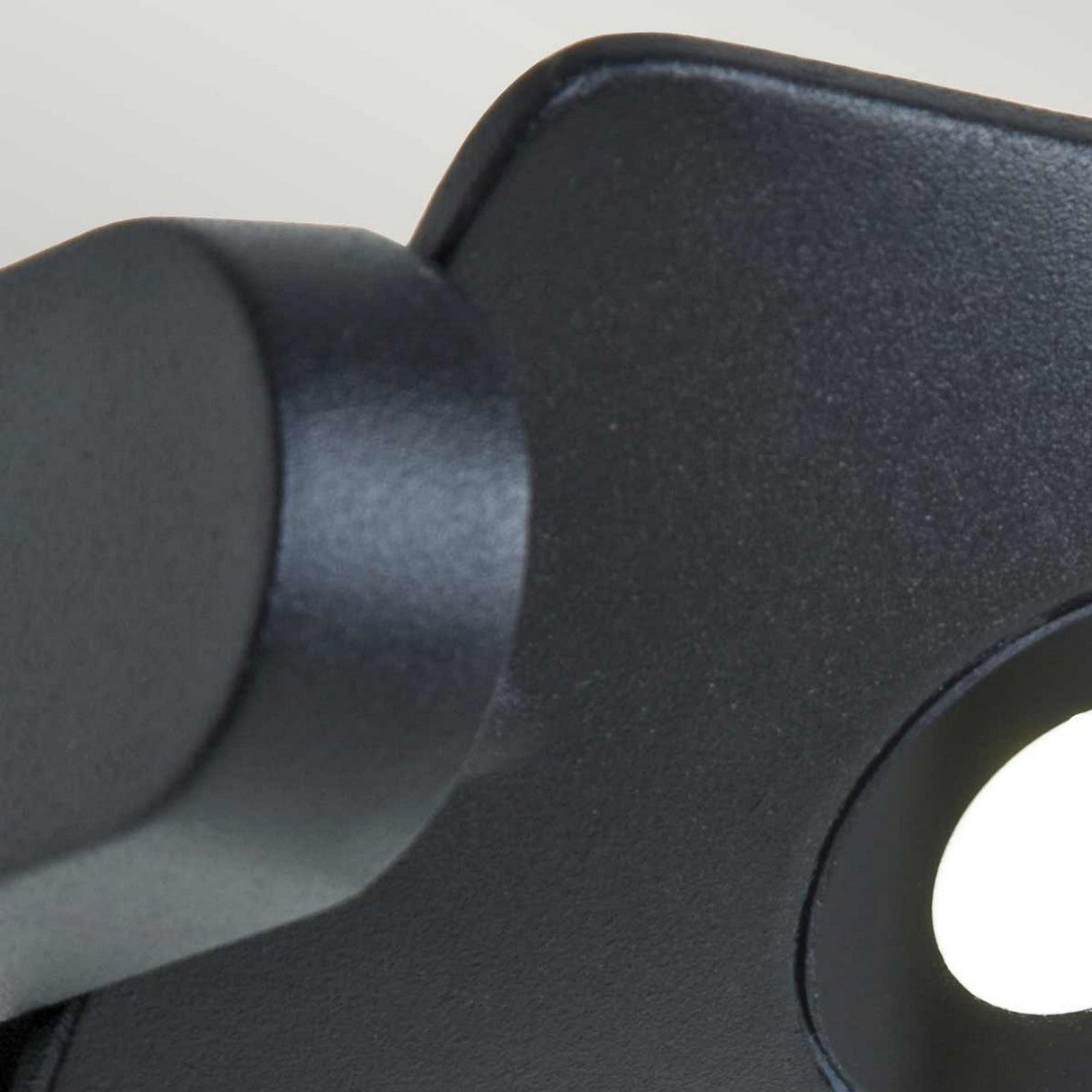 Close-up of the Sigmund 3 Light Outdoor Wall Light in graphite, showcasing a sleek, black metal design with a curved section and circular cutout. The blurred, light-colored background enhances its sophisticated and minimalistic appeal.