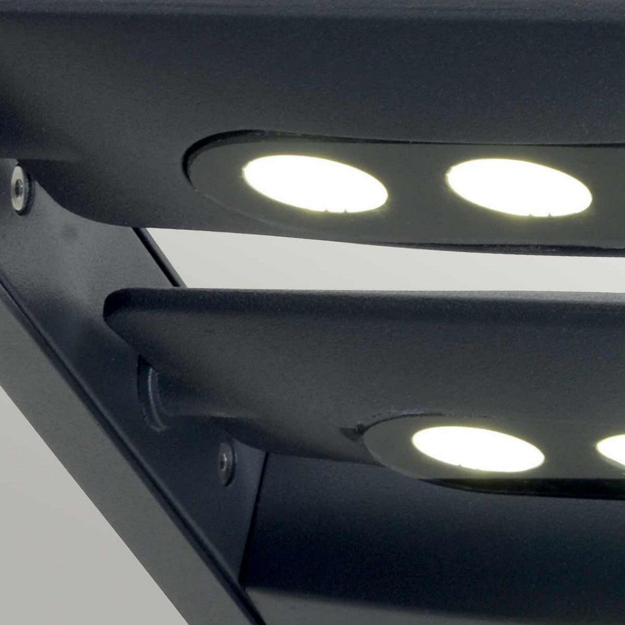 Close-up of the Sigmund 6 Light Outdoor Wall Light in Graphite, featuring a modern dark-colored LED light fixture with four illuminated circular lights. The design boasts sleek lines and a metallic finish, perfectly capturing a contemporary aesthetic for an advanced outdoor wall light with cutting-edge LED technology.