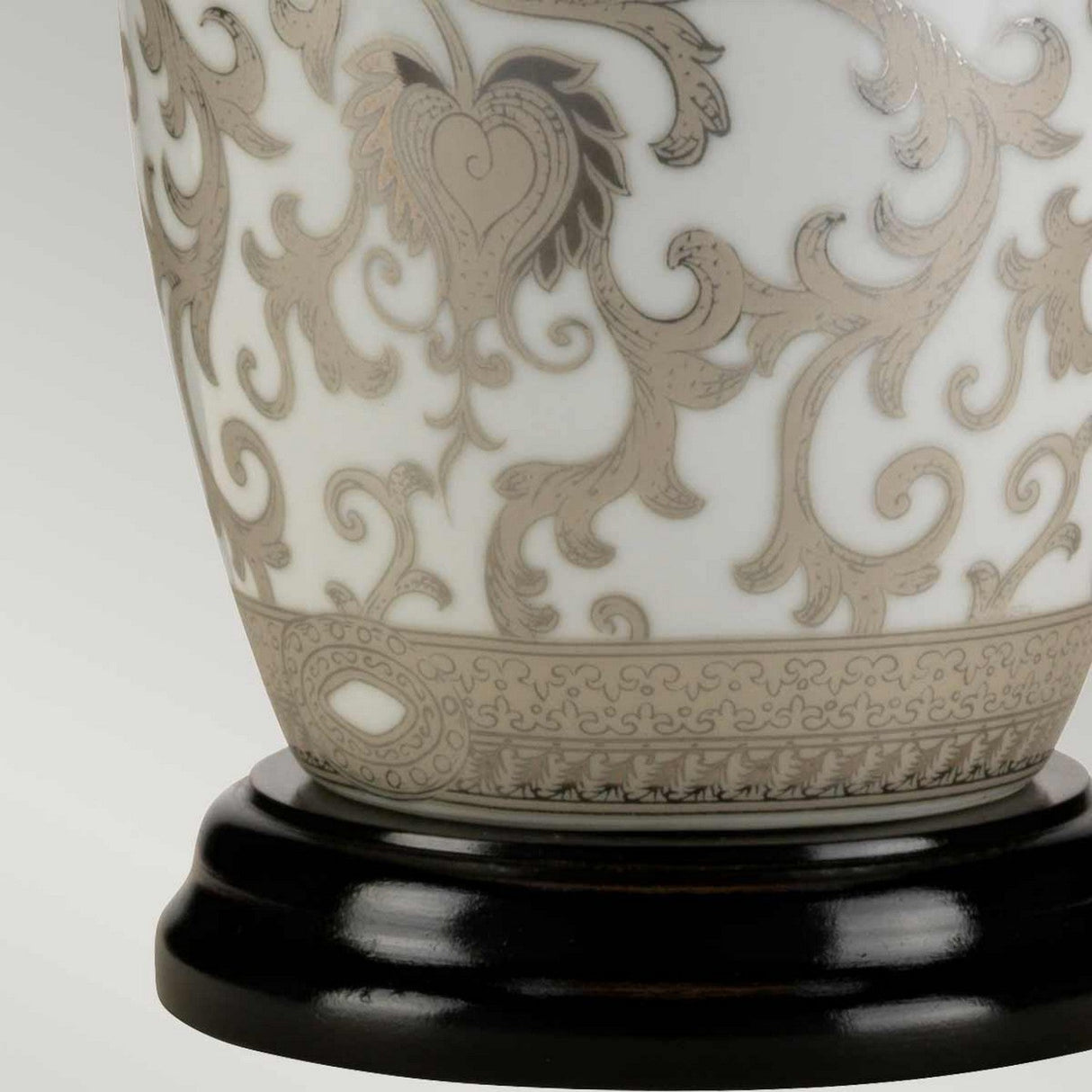 A close-up of the Silver Thistle 1 Light Table Lamp in white and silver, featuring intricate metallic floral patterns, adds an elegant touch as it rests on a glossy black wooden base.