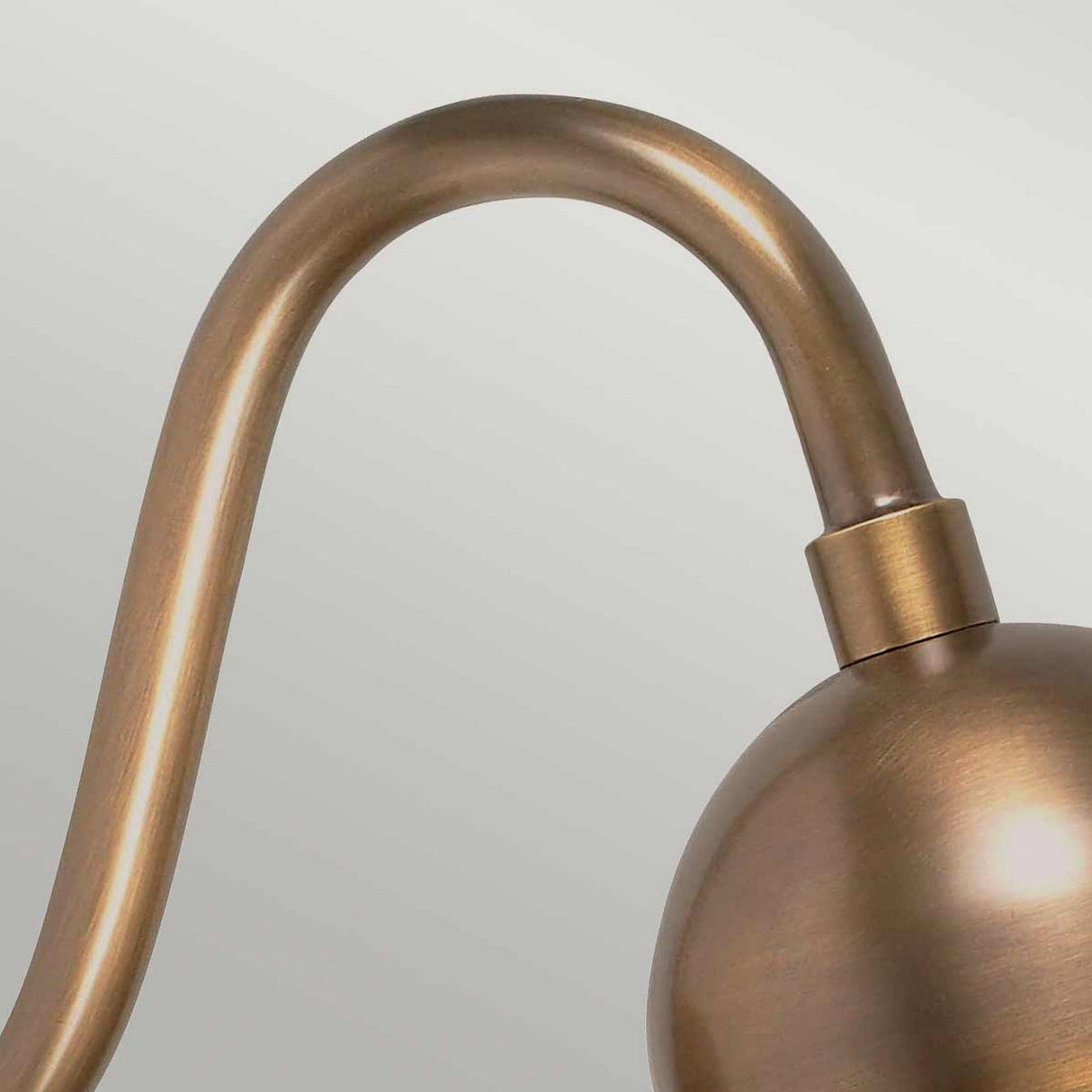 A close-up of the Somerton 1 Light Outdoor Wall Light in aged brass features a curved arm and a spherical shade, beautifully displayed against a light gray background.