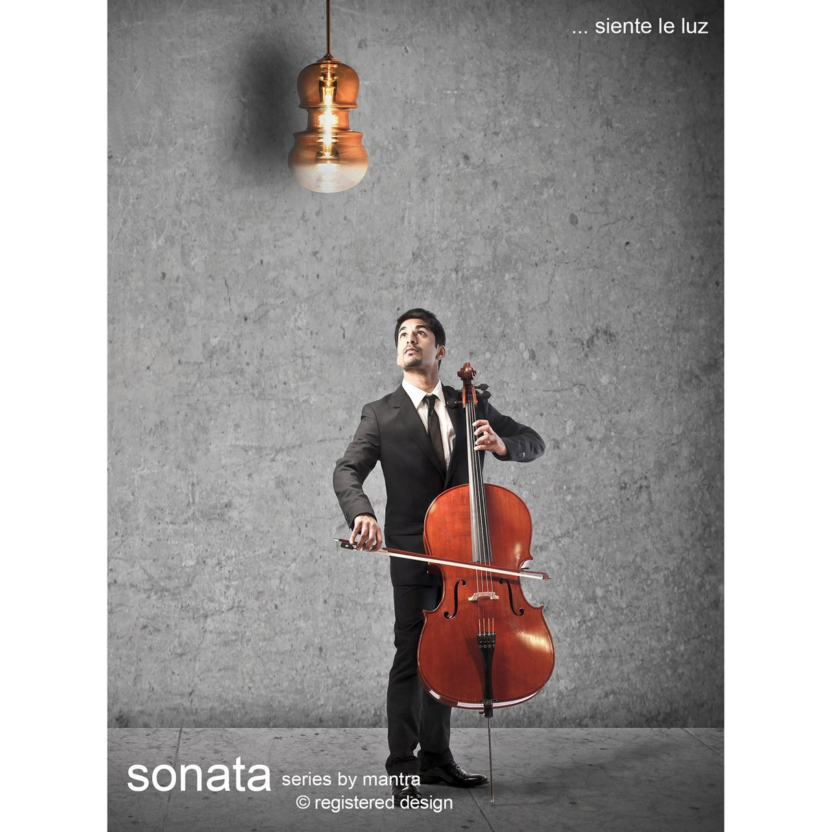 Mantra Sonata pendant light with hand-blown copper glass shade in a stacked double-bulb silhouette, lit above a cellist in a concrete-walled setting.