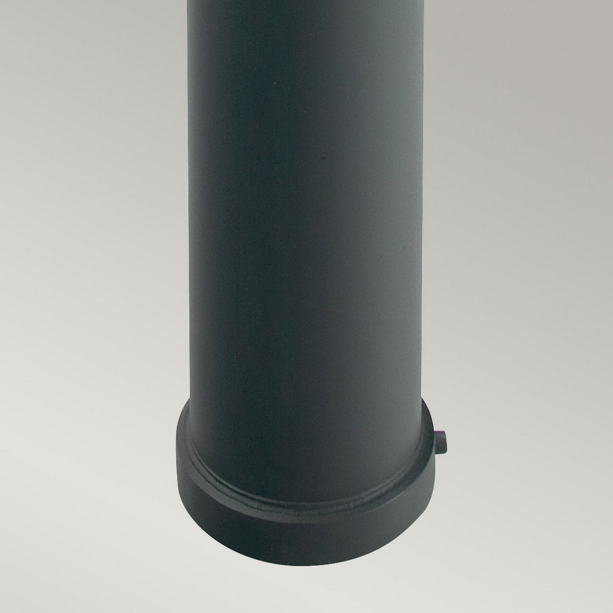 A close-up view of the Stockholm 1 Light Large Bollard - Black, its cylindrical form set dramatically against a gray background, possibly hinting at galvanized steel construction.