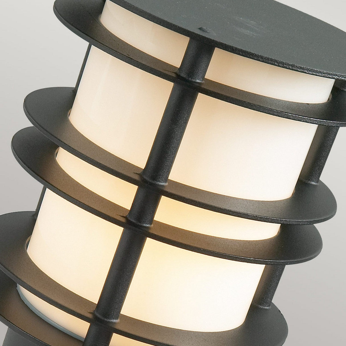 The Stockholm 1 Light Medium Bollard - Black showcases a Scandinavian design with a modern outdoor light fixture featuring a cylindrical shape. Encircled by horizontal metal bands and resembling a galvanized steel bollard, it offers a layered appearance while providing a soft, warm glow.