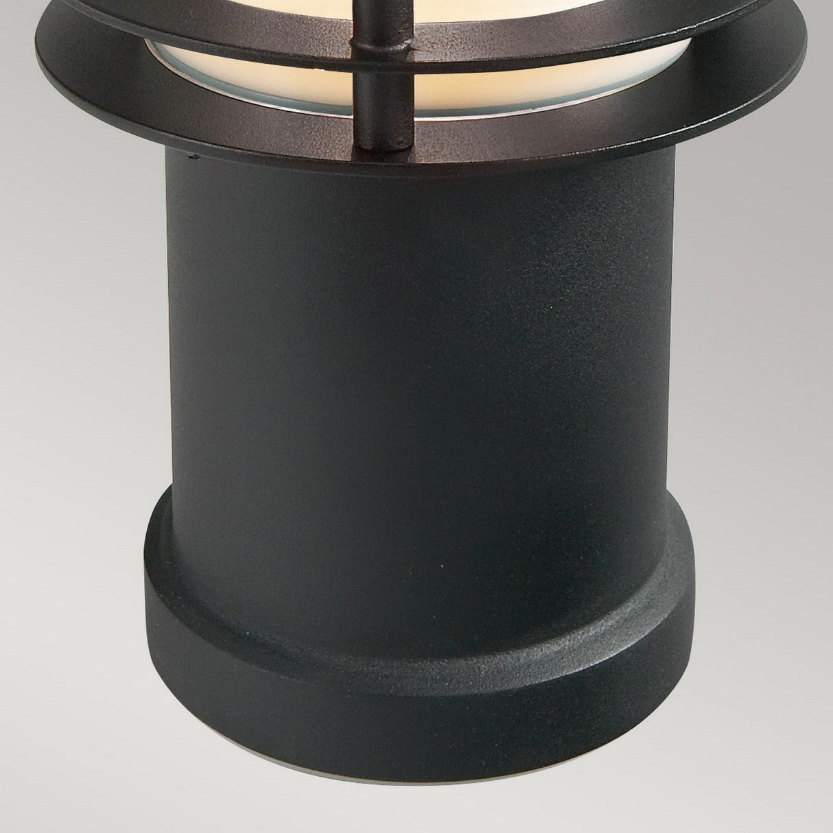 Close-up of the Stockholm 1 Light Small Bollard in black, featuring a Scandinavian design with a galvanized steel frame and frosted glass cover that emits a soft glow. The background is plain gray.