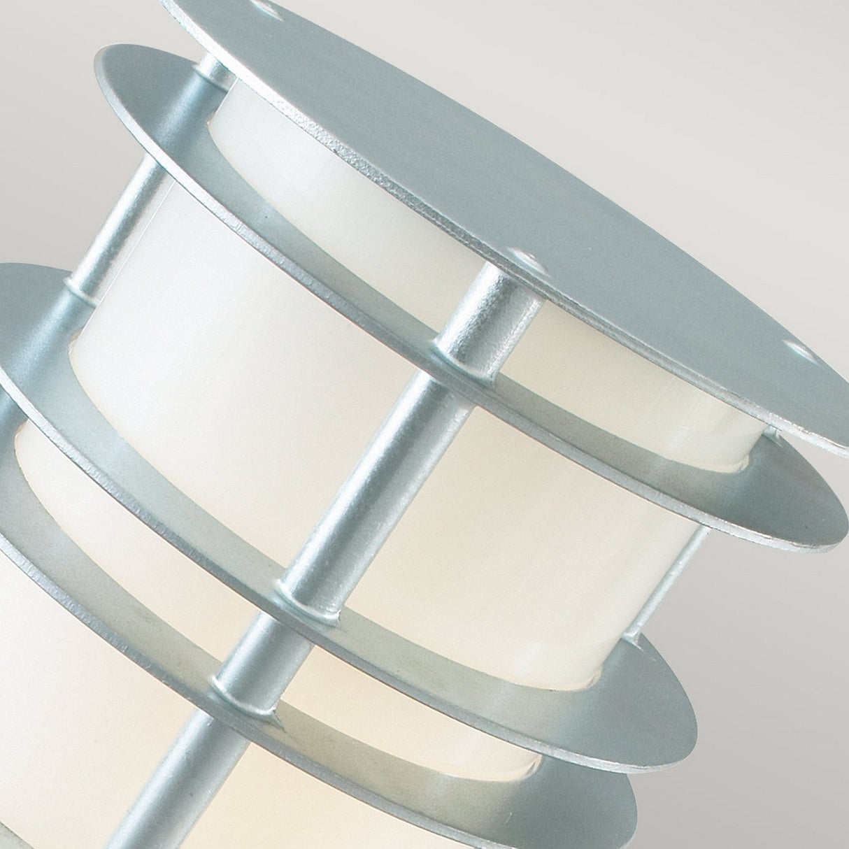 Close-up of the Stockholm Small Bollard - Silver, a modern outdoor lamp with a cylindrical shape, featuring galvanized steel rings and frosted glass sections. This elegant piece of lighting is set against a light gray background, embodying sleek modern design.
