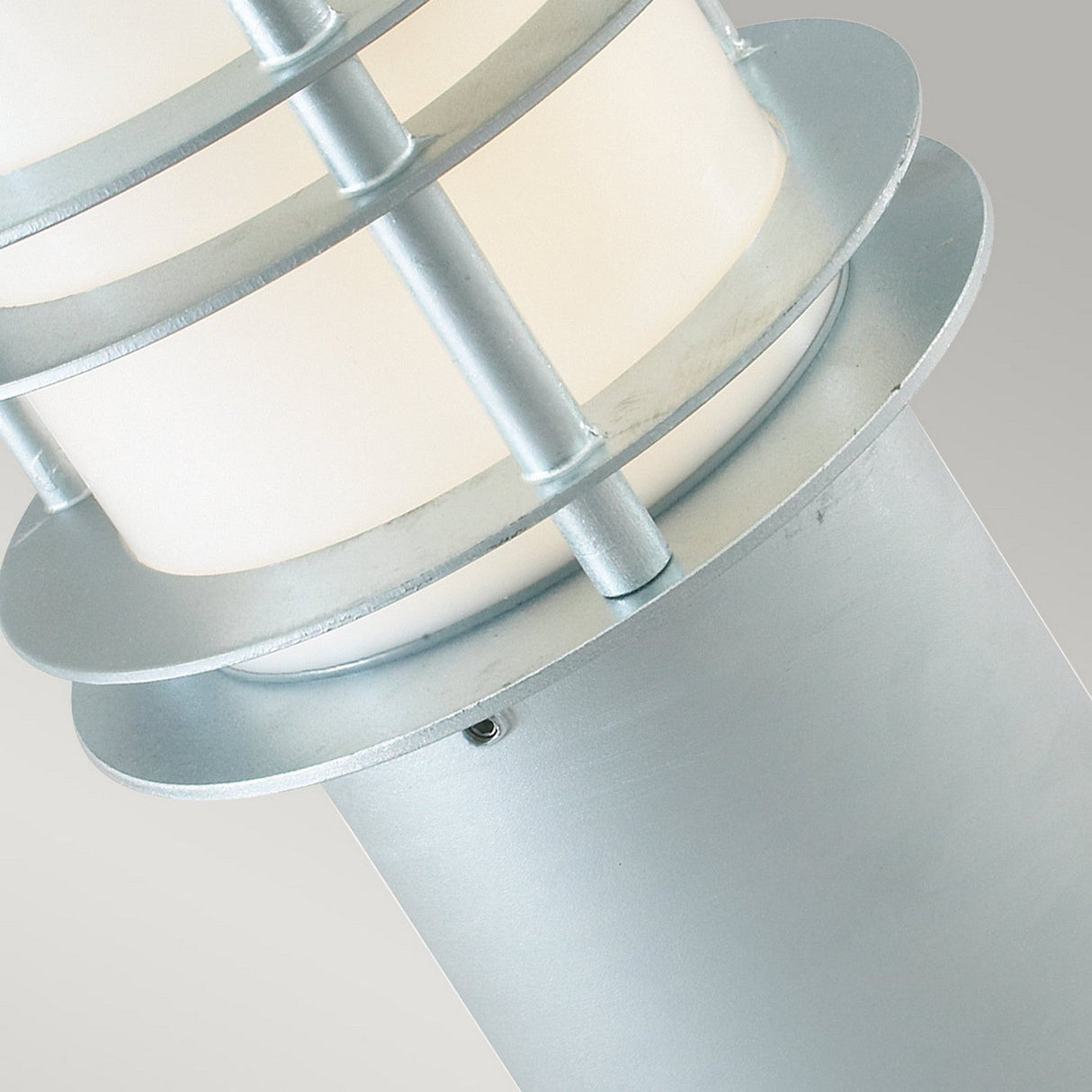 Close-up of the Stockholm Small Bollard - Silver, highlighting its sleek outdoor lighting design with a silver metallic structure crafted from galvanized steel and horizontal bands. The frosted white glass shade stands out against the plain, light gray background.