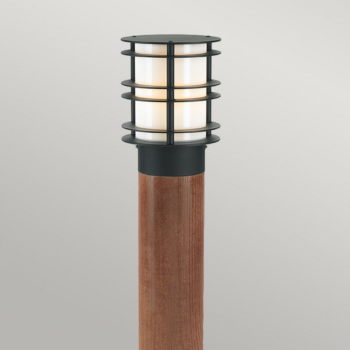 The Stockholm Large Bollard Stained Wood - Black is a modern outdoor light fixture with a black metal cage enclosing a cylindrical white light, elegantly set against a plain, light gray background.