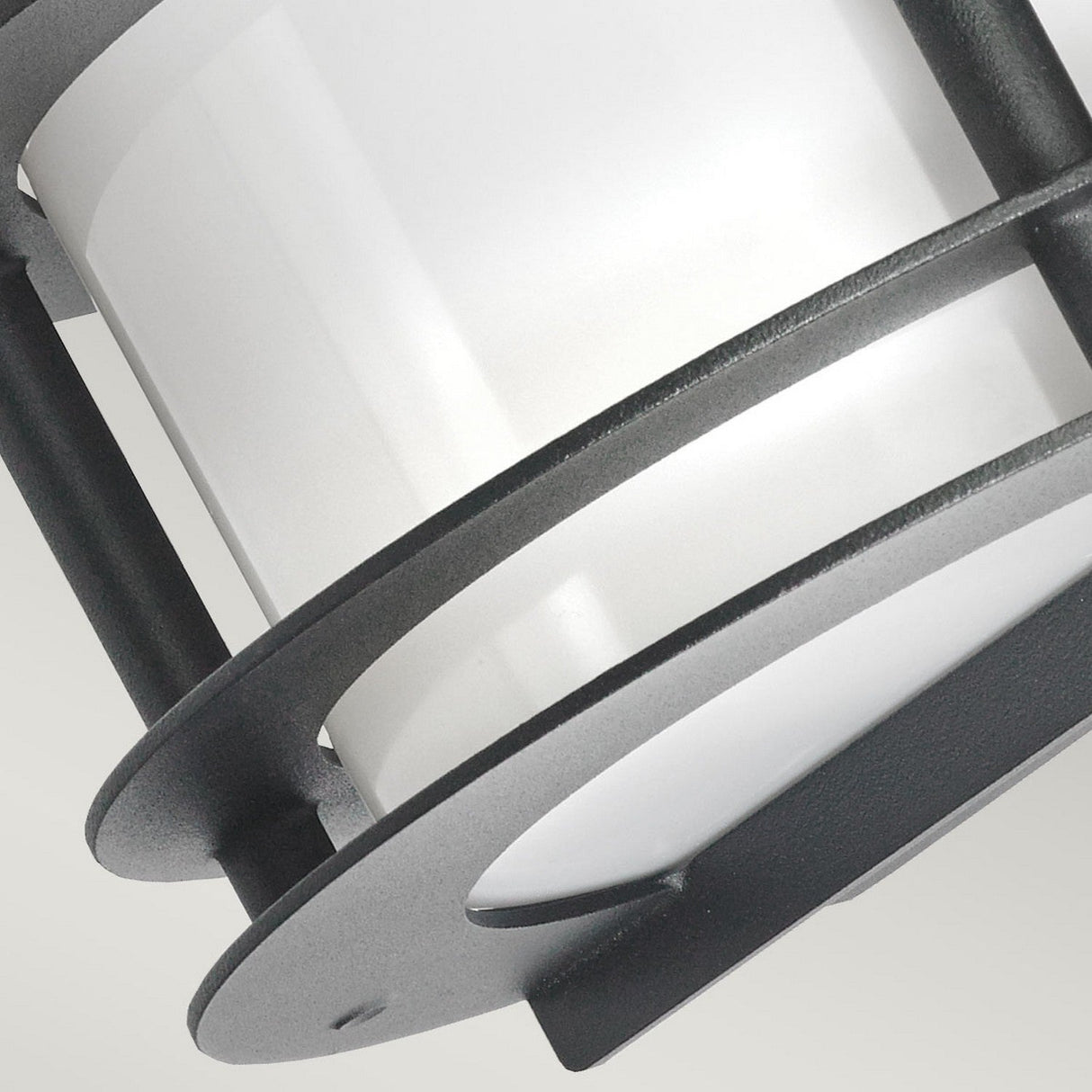 Close-up of the Stockholm Outdoor 1 Light Flush Light in black, featuring a modern and corrosion-resistant design with an opal glass cylindrical shade, encased in a sleek metal frame with circular bars, embodying a minimalist and industrial style.