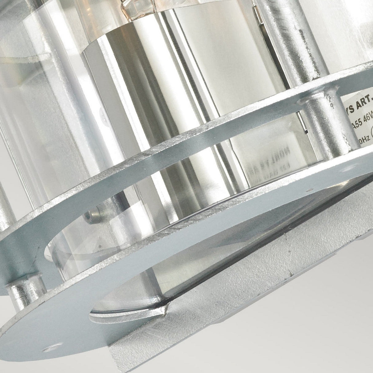 The image features a close-up of a cylindrical structure crafted from galvanized steel and equipped with transparent sections, showcasing industrial elements and engraved text. This IP54-rated depiction highlights the intricate details of the Stockholm Outdoor 1 Light Flush Light in silver with clear glass against a light background.