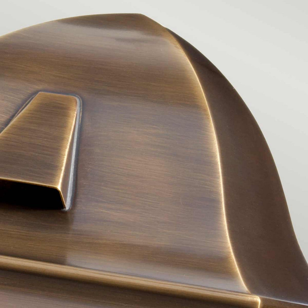 Close-up of the St James 1 Light Outdoor Wall Light in aged brass, highlighting its smooth, angled surfaces and matte finish. The geometric design with a pointed segment and overlapping layers embodies the sleek sophistication characteristic of British design.