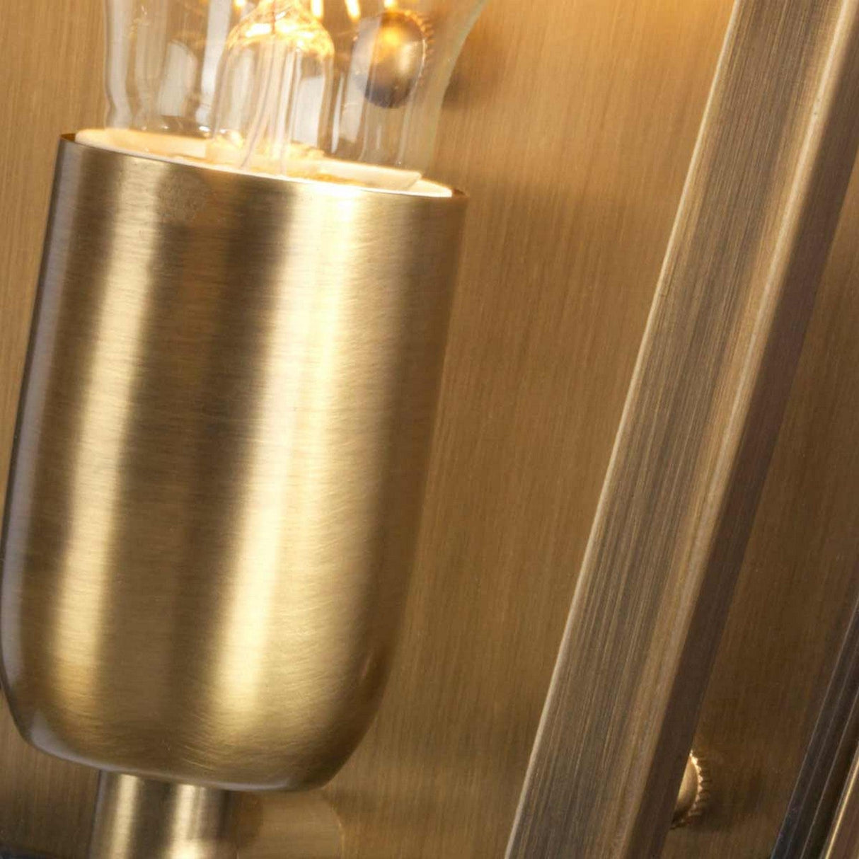 Close-up of the St James 1 Light Outdoor Wall Light in aged brass, showcasing British design flair. The visible light bulb complements the brushed metal background, highlighting its smooth, polished surface and warm, aged brass tone.
