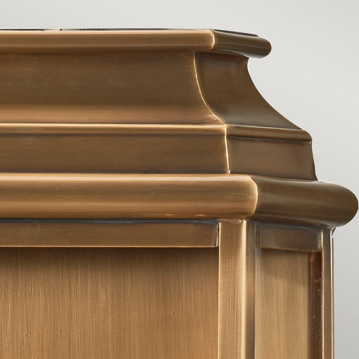 Close-up of the top corner of a St Martins 2 Light Outdoor Large Wall Light in aged brass with decorative molding, exuding historical charm. The surface appears smooth and well-polished, highlighting subtle variations in texture and color reminiscent of aged brass.