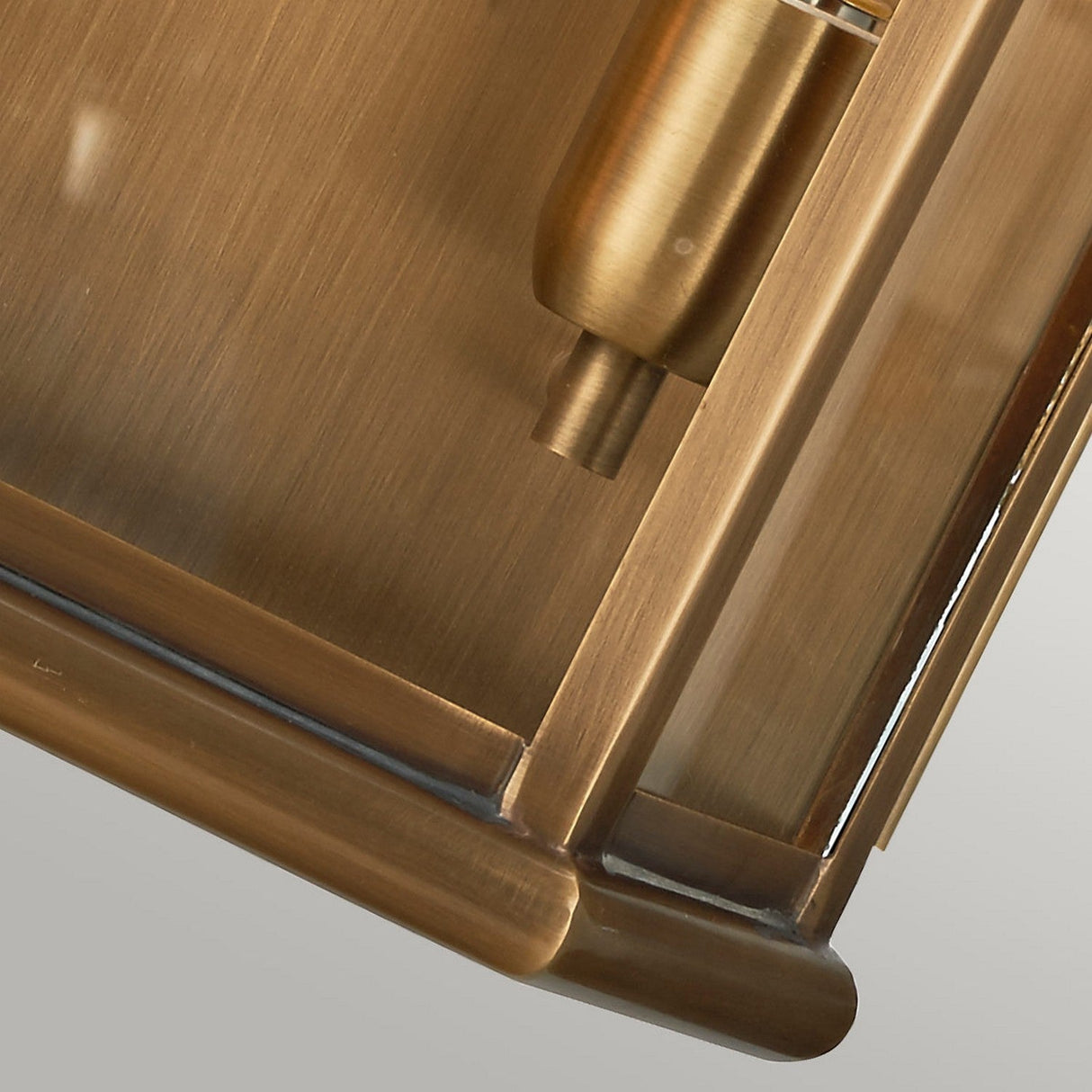 Close-up of the St Martins 2 Light Outdoor Large Wall Light in aged brass, featuring a metal and glass structure. The image reveals a smooth, reflective surface with a partially visible cylindrical component at the top. The angled view accentuates the intricate details and historical charm of its craftsmanship.