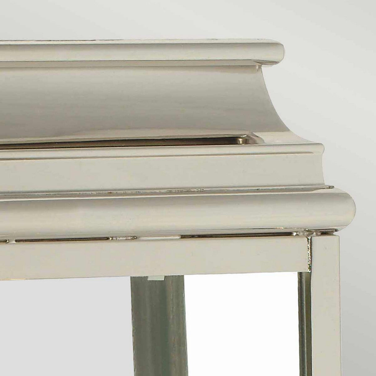 Close-up of a metallic silver corner resembling the St Martins 1 Light Outdoor Wall Light in polished nickel. The top section is curved, giving it a classic and elegant look, and the mirror reflects a soft, neutral background.