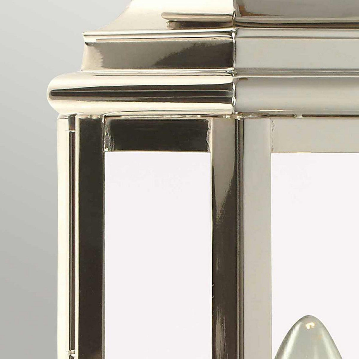 A close-up of the St Martins 1 Light Outdoor Wall Light in polished nickel reveals its shiny, metallic frame with reflective surfaces and a glimpse of a white candle inside. The neutral gray background highlights the lustrous texture of the frame.