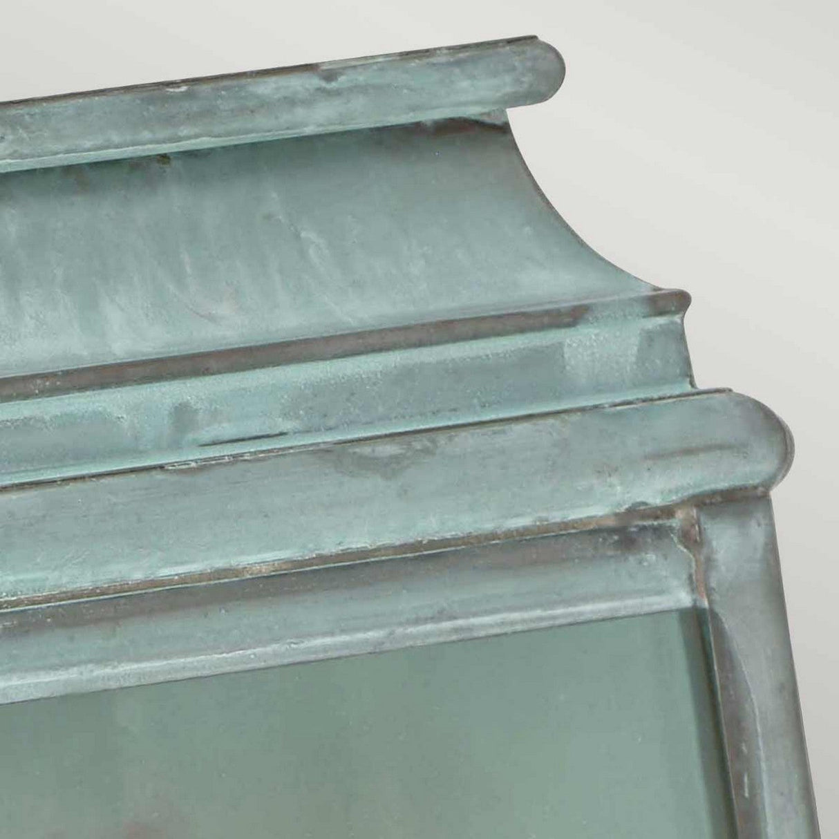 Close-up of the St Martins 1 Light Outdoor Wall Light in Verdigris, featuring a weathered, green patina metal structure with layered edges and a slightly curved surface. Set against a light gray background, the texture suggests age and exposure to the elements.