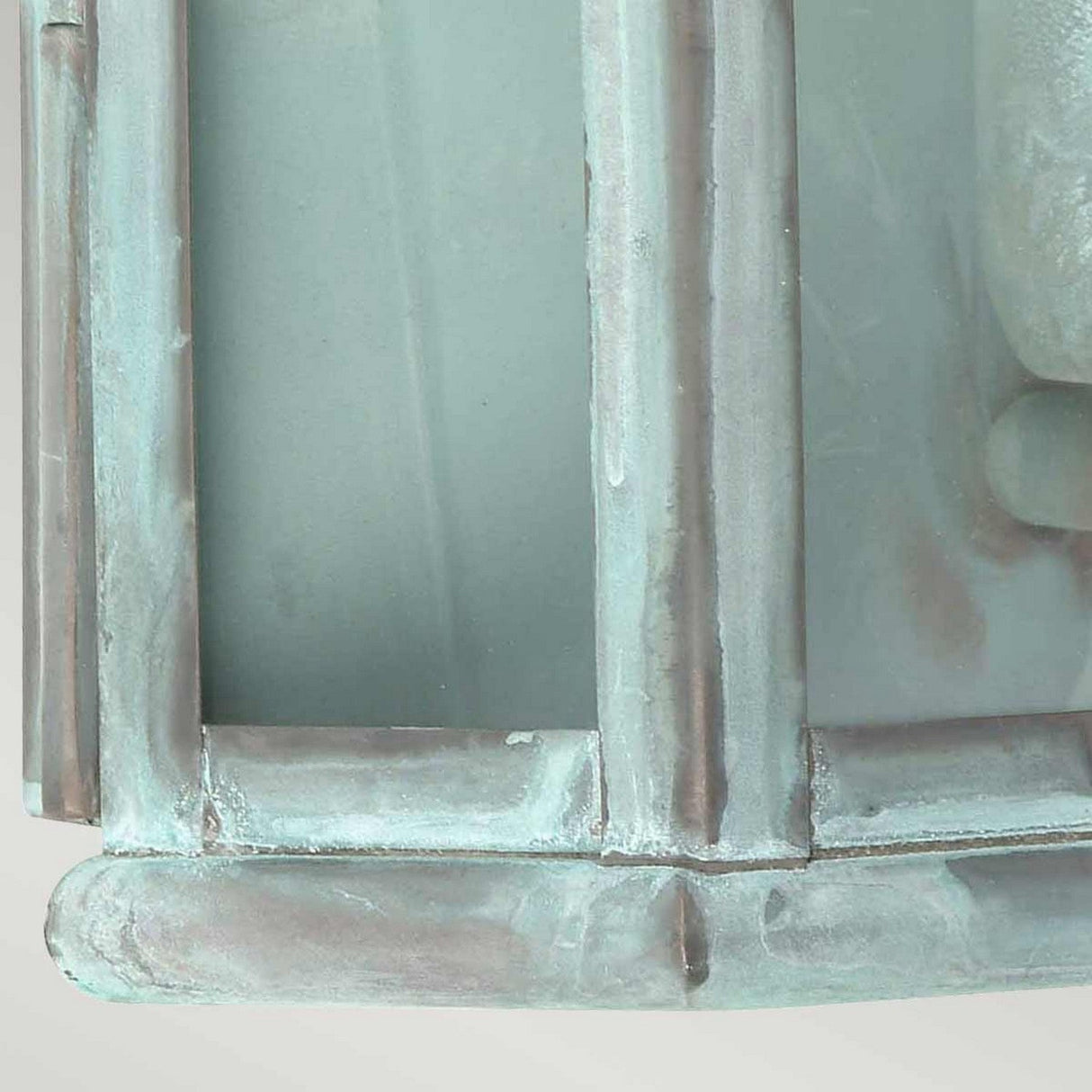 A close-up of the St Martins 1 Light Outdoor Wall Light in Verdigris showcases its light green, rectangular grid structure. Constructed to mimic metal or glass, it features intersecting horizontal and vertical bars forming square panels. The surface has a slightly weathered, matte finish that enhances its outdoor wall light design.