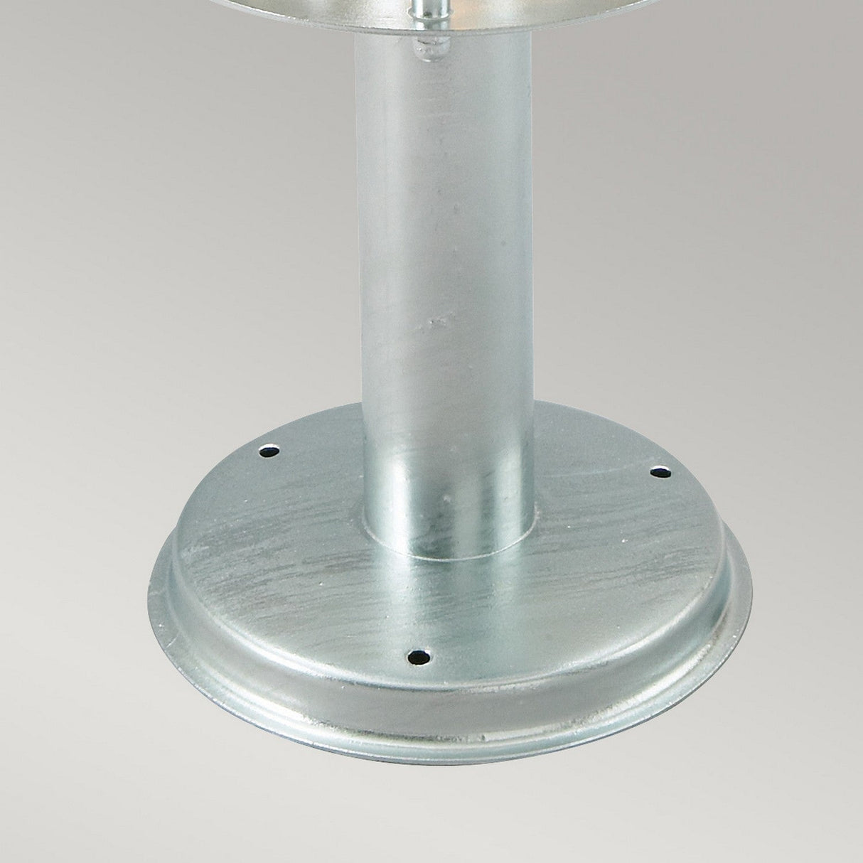 A close-up view showcases the Stockholm 1 Light Grande Pedestal - Silver, featuring a metallic round base crafted from galvanized steel with a cylindrical pole extending upwards. This pedestal includes four small, evenly spaced holes near the edge for mounting, and its sleek, smooth surface reflects the hallmark of Scandinavian design.