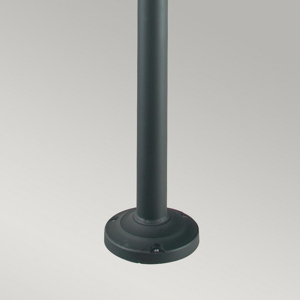 A close-up image of the base of a dark-colored vertical metal pole standing on a plain, light gray background. The Stockholm 2 Light Twin Lamp Post - Black boasts a cylindrical pole and a slightly elevated circular base, reflecting Scandinavian-inspired design principles.