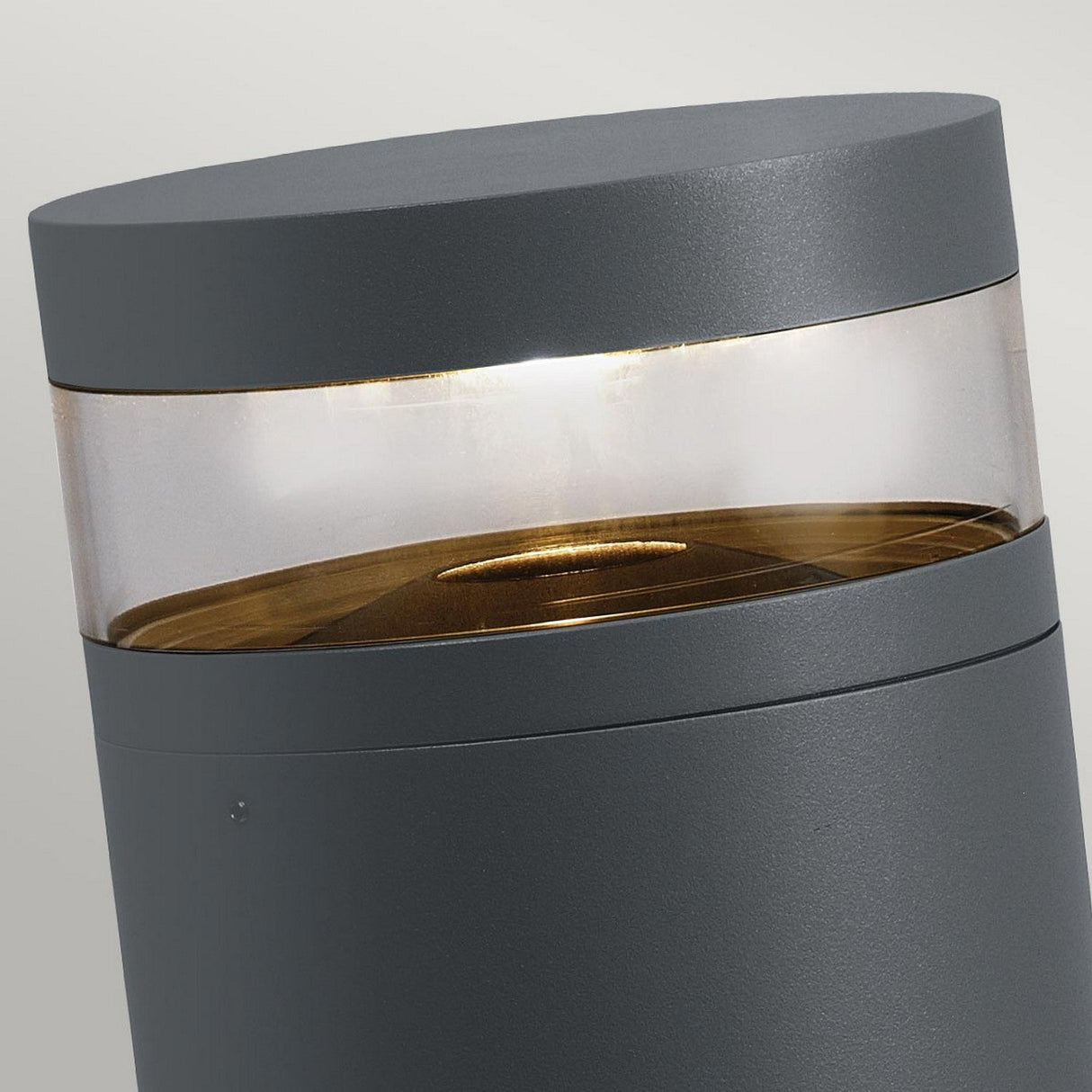 Introducing the Stavanger LED Medium Bollard in Graphite, a contemporary cylindrical lamp featuring a transparent middle section that showcases its internal light source. This lamp offers a sleek and minimalist design with a smooth graphite finish, perfect for outdoor lighting. Its weather-resistant qualities ensure it remains durable under any condition.