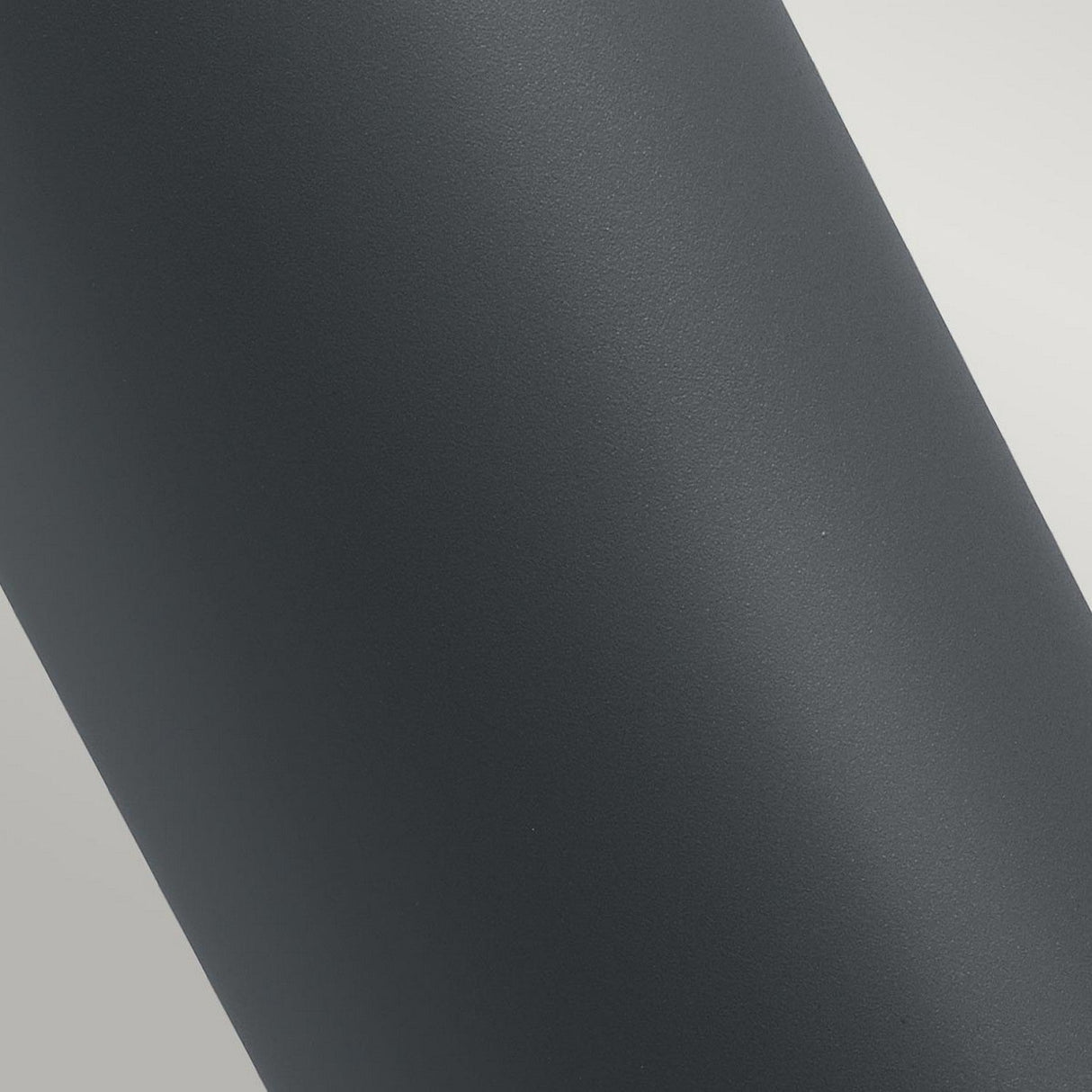 A close-up of the Stavanger LED Medium Bollard in graphite reveals its sleek, cylindrical design. The lighting highlights its texture and curvature, emphasizing its weather-resistant design, perfect for outdoor lighting.