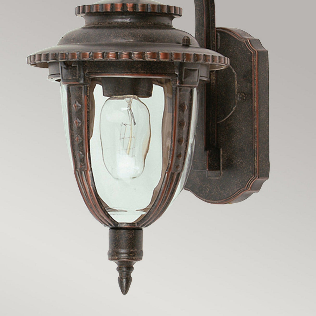 The St Louis 1 Light Outdoor Medium Wall Light features a vintage design, highlighted by hand-blown glass that reveals a visible light bulb inside. It is crafted with a weathered bronze finish on the frame and decorative edges, elegantly mounted on a flat backplate.