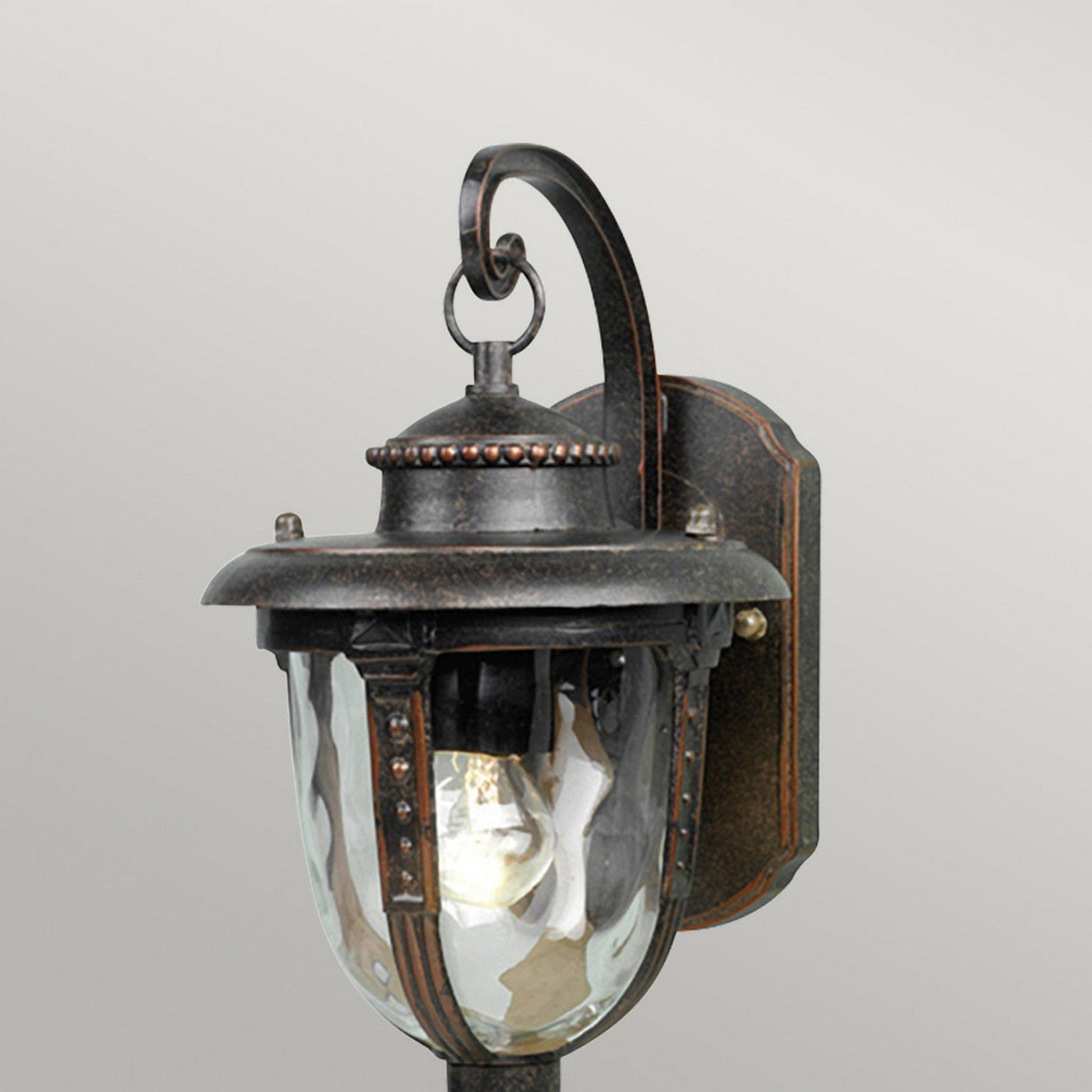 The St Louis 1 Light Outdoor Small Wall Light in weathered bronze showcases a vintage-style design with a metal frame and hand-blown glass shade. It features a decorative curved arm and mounts on a wall plate against a plain background.