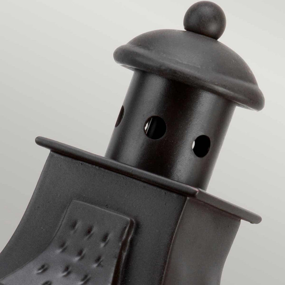 Close-up of the Stow 1 Light Outdoor Wall Light in Old Bronze, showcasing a black metal top with a rounded cap and circular cut-out holes for ventilation. The design features a slightly curved body with a textured surface, giving it an antique appeal and classic, rustic appearance.