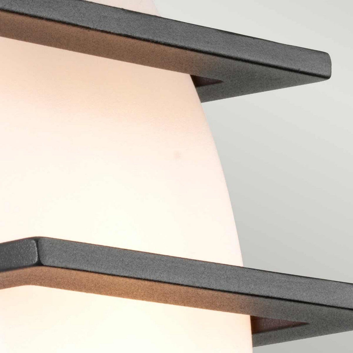 Close-up of the Sven 1 Light Outdoor Wall Light - Graphite, showcasing its frosted white glass shade and horizontal dark graphite bands against a light gray background. With an IP65 rating, this design presents angular, sleek lines for a contemporary aesthetic.