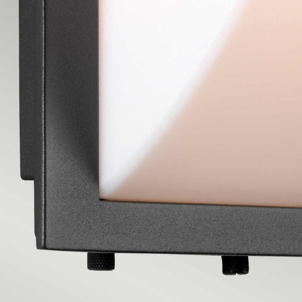 A close-up of a black metal frame corner showcases the sturdy design reminiscent of the Sven 1 Light Outdoor Wall Light - Graphite, featuring two small protruding knobs around a beige and white textured surface. The light gray background accentuates its graphite-like finish.