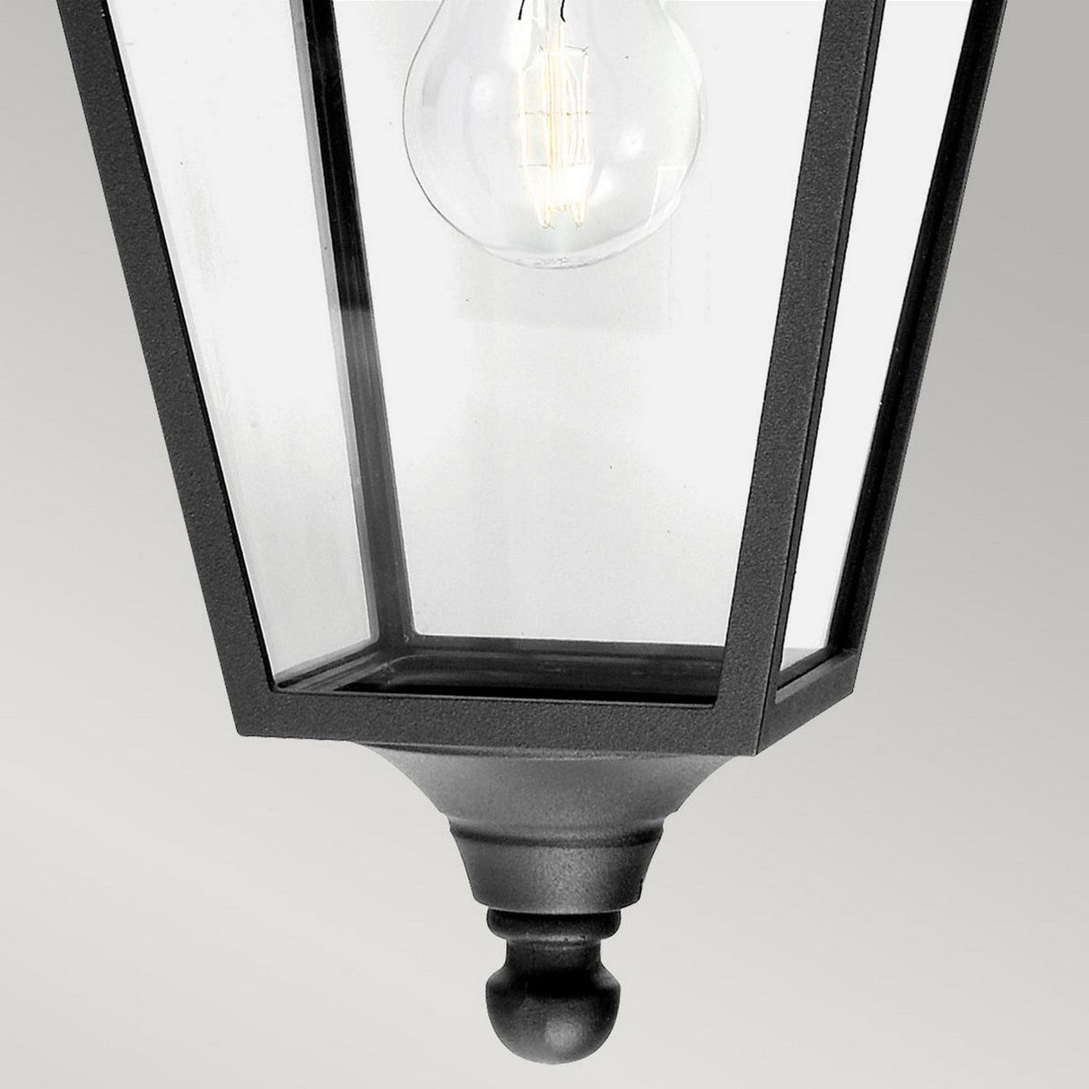 A close-up of the Turin Outdoor 1 Light Down Wall Lantern in black showcases its classic tapered design with a visible incandescent bulb encased in glass and supported by a die-cast aluminium frame, set against a light gray background.