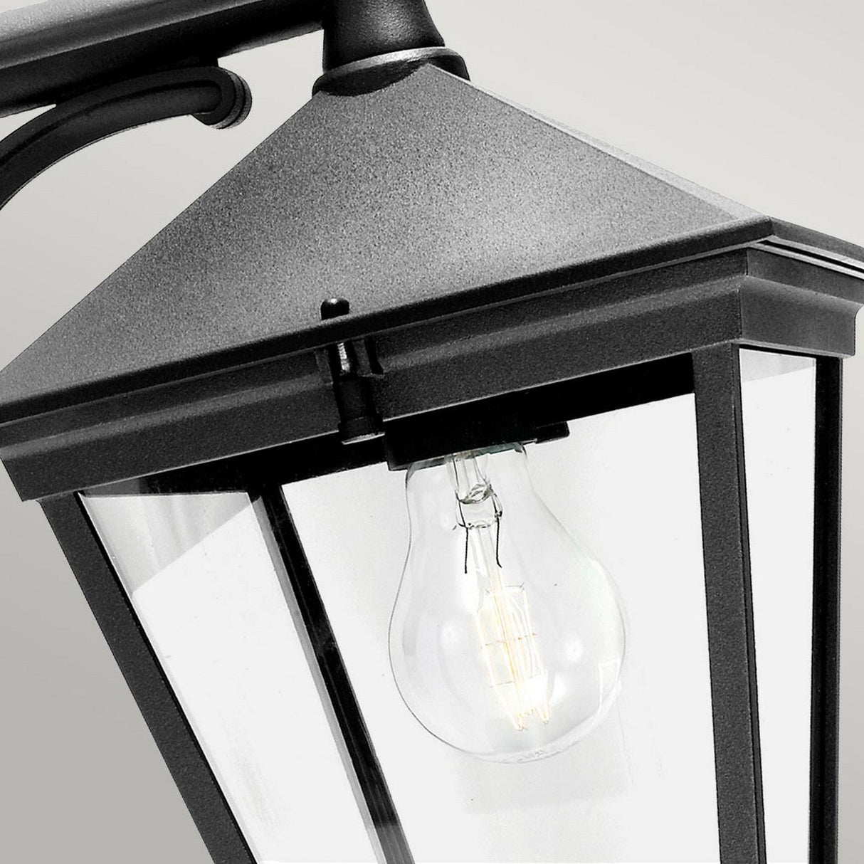 Close-up view of the Turin Outdoor 1 Light Down Wall Lantern in black, crafted from die-cast aluminum. It features a clear glass enclosure showcasing a visible incandescent bulb inside. The lantern's classic, angular design is complemented by its sturdy IP54 rating, set against a neutral gray background.