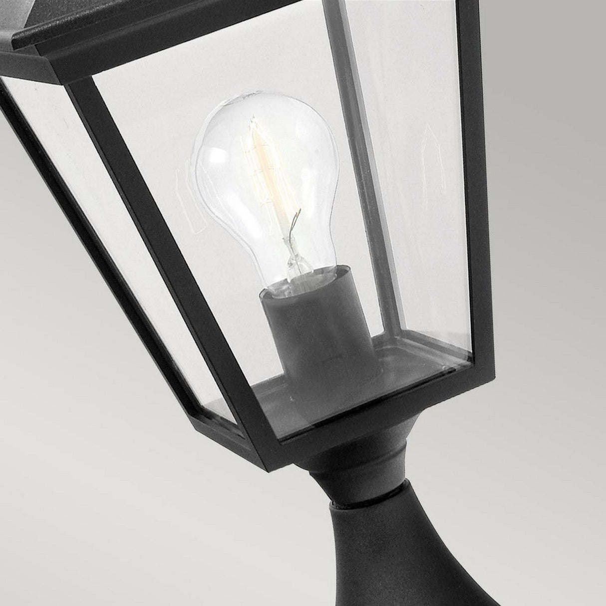 Close-up of the Turin 1 Light Pedestal in black, expertly crafted from durable die-cast aluminum and featuring a clear glass enclosure that reveals a visible light bulb inside. This outdoor lighting fixture boasts an IP54 rating and is set against a plain, light gray background.