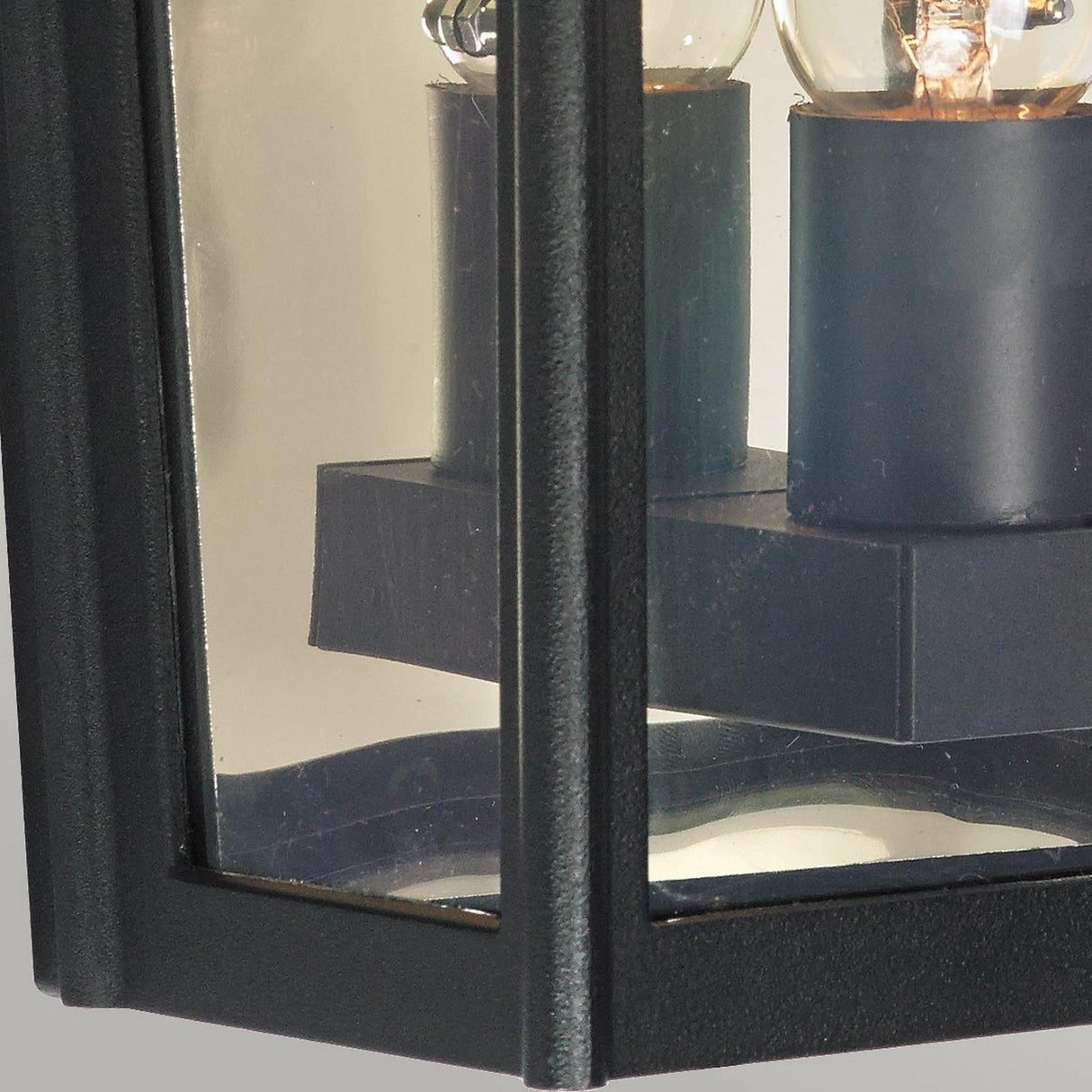 Close-up of the Turin Outdoor 1 Light Half Wall Lantern in die-cast aluminium with a black-framed glass design, showcasing two visible light bulbs inside. This modern and sleek outdoor wall lantern is partially shown against a plain background and features an IP54 rating for enhanced durability.