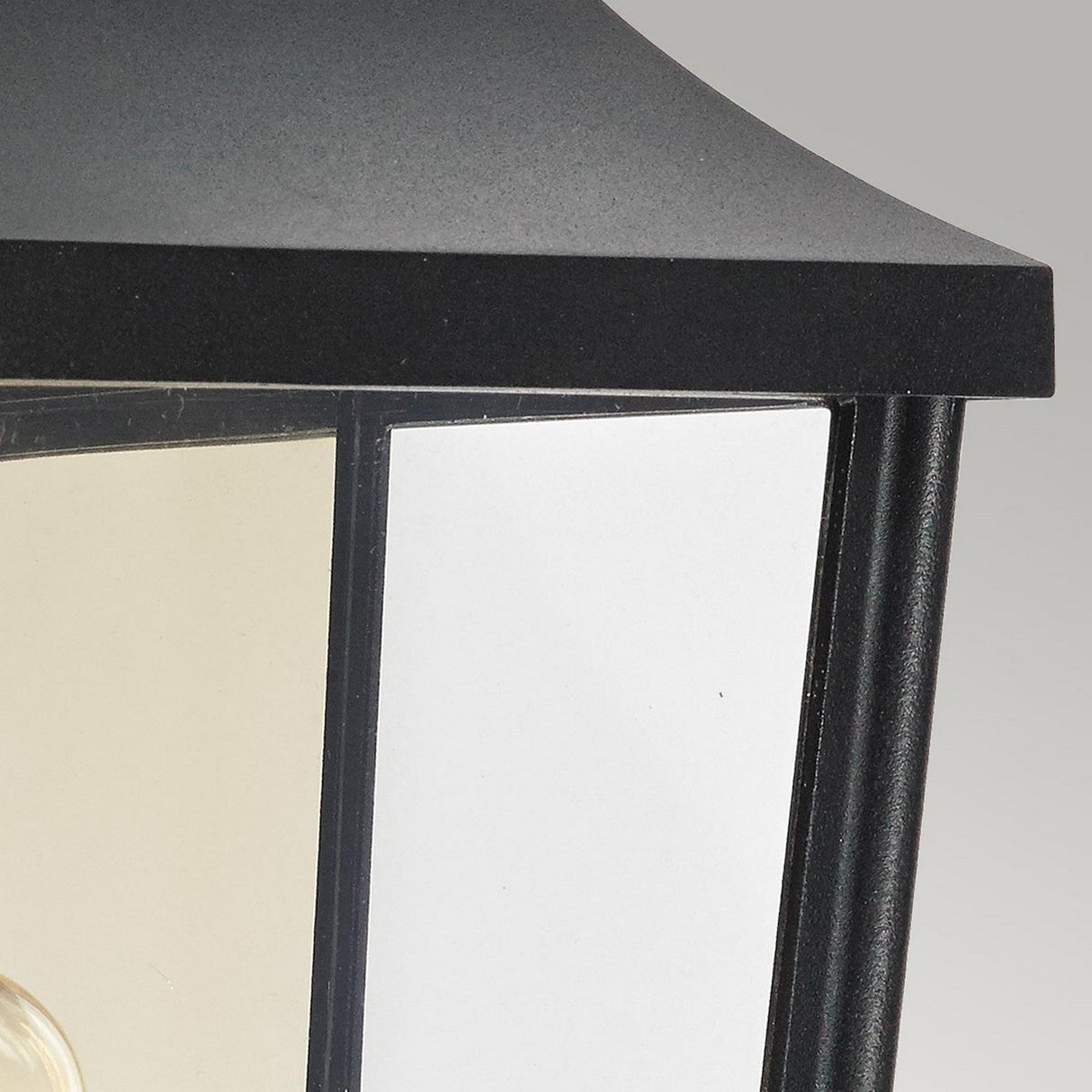 Close-up of the Turin Outdoor 1 Light Half Wall Lantern - Black, featuring a black-framed design crafted from die-cast aluminum with clear glass panels. The top is angled and dark against a light background, and this stylish piece offers an IP54 rating for enhanced durability against the elements.
