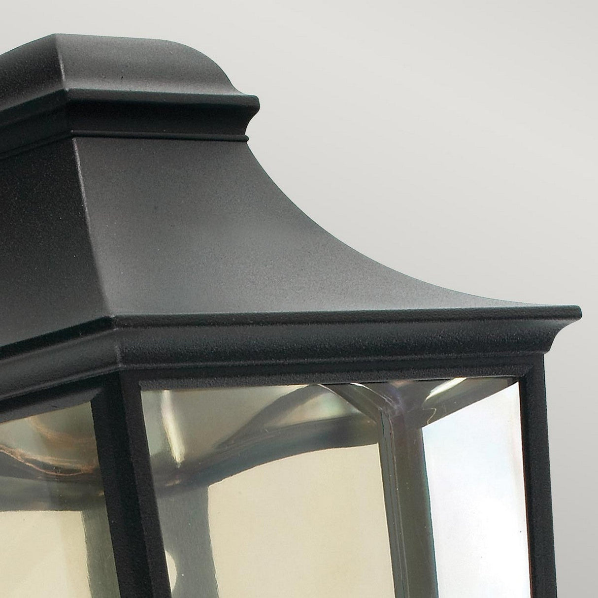 A close-up of the Turin Outdoor 1 Light Half Lantern in black showcases its die-cast aluminum construction with a glass panel set against a light gray background. The classic rectangular design features a gently curved top and offers an IP54 rating, ensuring its durability in any weather condition.