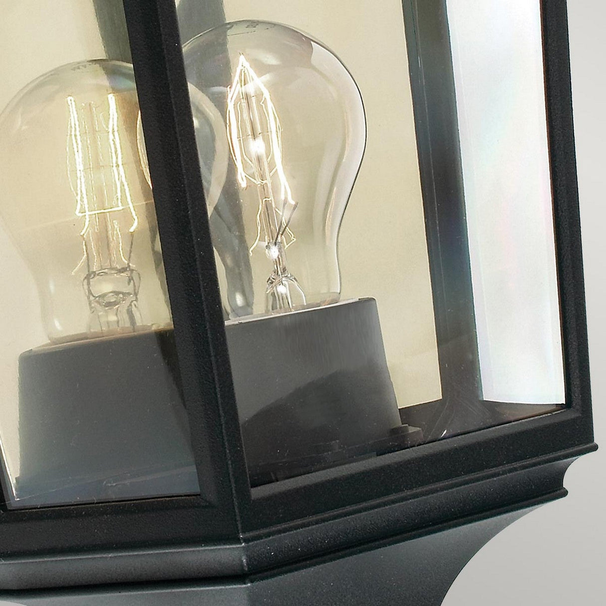 Close-up of the Turin Outdoor 1 Light Half Lantern in black, featuring transparent glass panels and crafted from die-cast aluminum. It showcases two clear light bulbs inside—one with a traditional incandescent shape and the other elongated.
