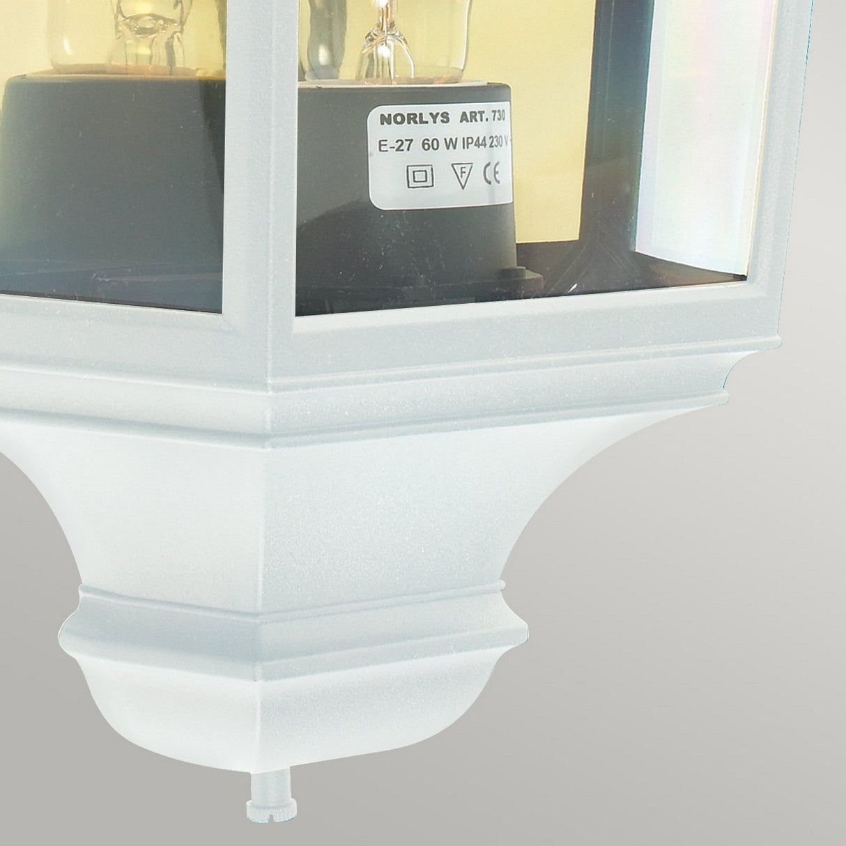 A close-up of the Turin Outdoor 1 Light Half Lantern in white highlights its die-cast aluminum construction with a glass enclosure. The fixture's elegant half lantern design is emphasized against a neutral gray backdrop. Inside, a light bulb is paired with specifications such as 60W and E-27 clearly labeled, showcasing the fixture's refined simplicity.