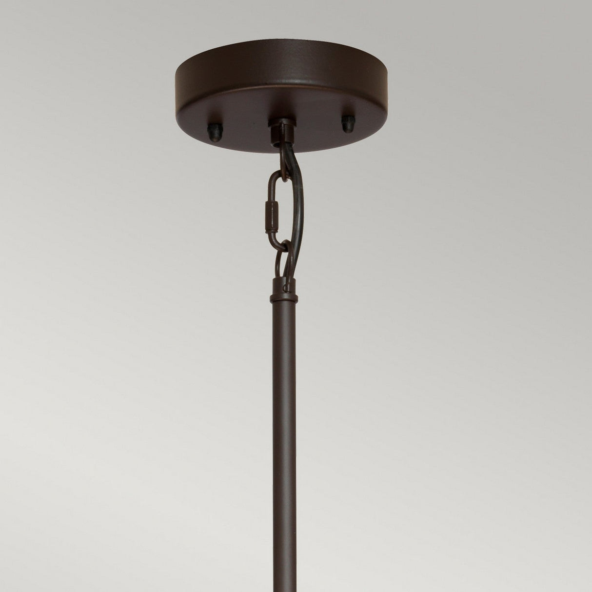 A close-up image showcases the Taiko 4 Light Chandelier - Olde Bronze, ceiling-mounted with a round base and straight rod. The rod is attached to the base using a small chain and hook, and the fixture is adorned with a neutral linen shade. The background features a plain, light gray color.