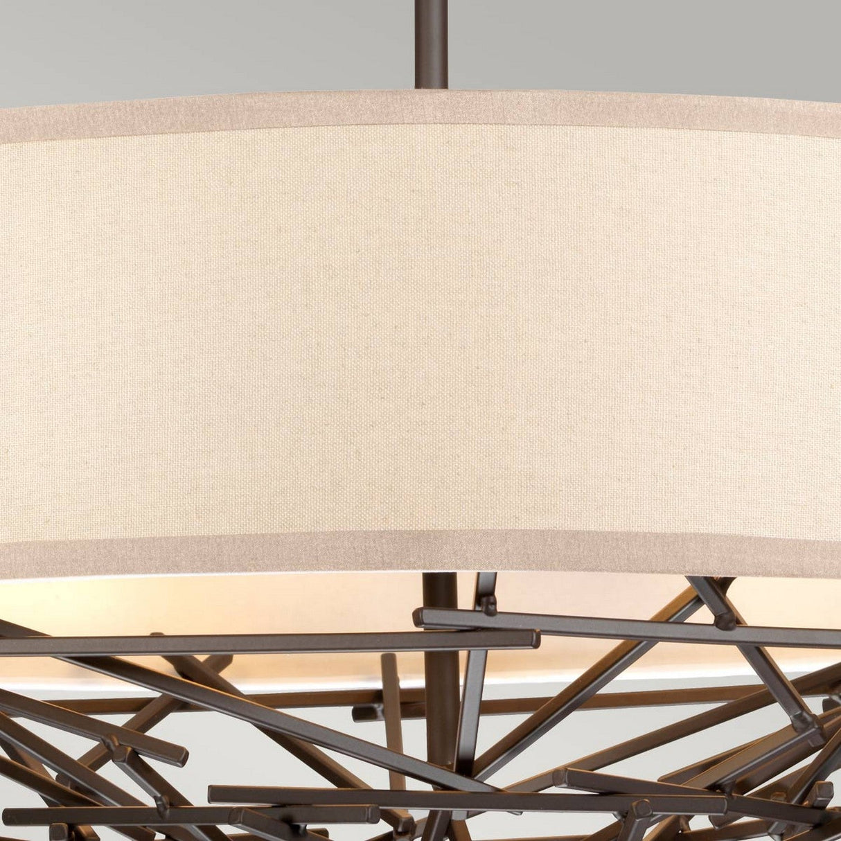 Close-up of the Taiko 4 Light Chandelier - Olde Bronze, showcasing its neutral linen shade and an interwoven metal frame with a geometric design, set against a gray background.