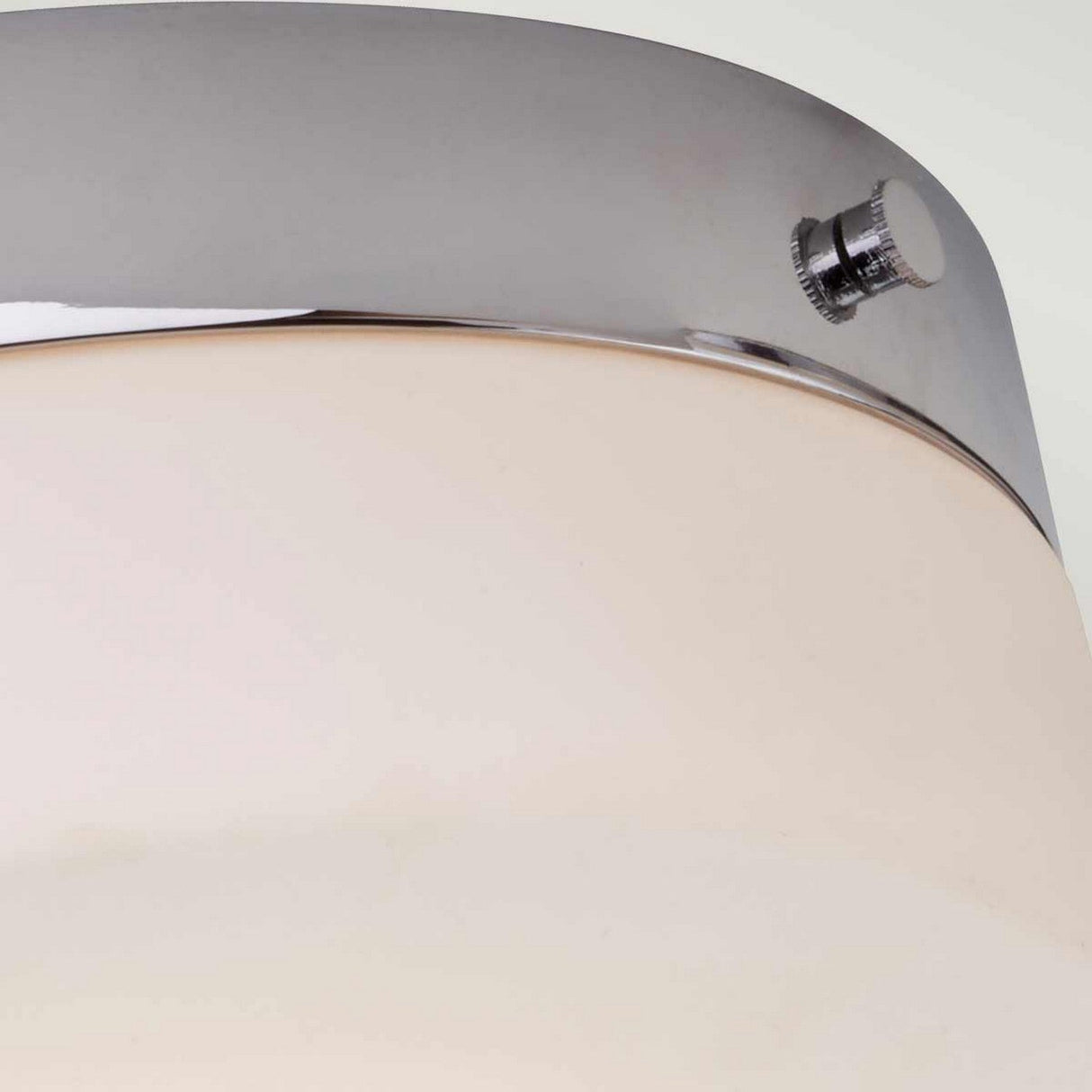 Close-up of the *Tamar 1 Light Large Flush - Polished Chrome*, showcasing its modern design with a polished chrome metal finish and a frosted white glass shade. A small knob embellishes the metal fixture against a light gray background, accentuating the sleek elegance of this LED lamp.