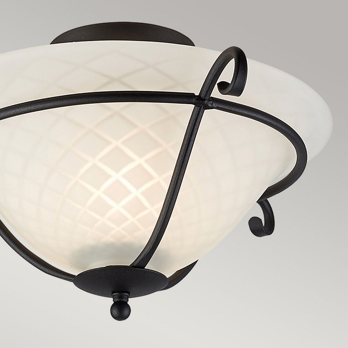 Close-up of the Torchiere 1 Light Flush, showcasing opal etched glass with a crisscross pattern. This light fixture is supported by a black metal frame adorned with curved accents, exuding Gothic charm, set against a plain gray background.