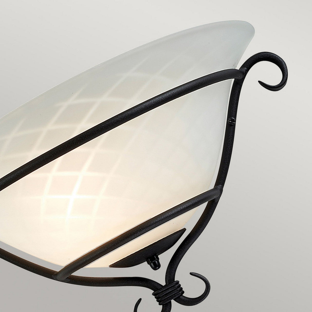 The Torchiere 1 Light Wall Uplighter - Black With Etched Opal Glass showcases an elegant etched opal glass lampshade adorned with a diamond pattern, supported by a black metal frame with curved accents, radiating Gothic elegance as it is gently illuminated against a neutral background.